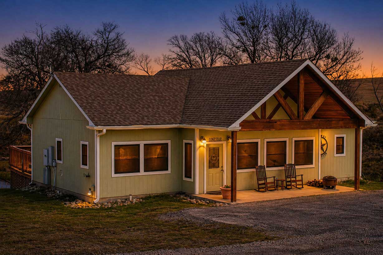 Lonestar cabin at Willowood Ranch with porch lights on at twilight, featuring rustic wood beams and a peaceful countryside setting