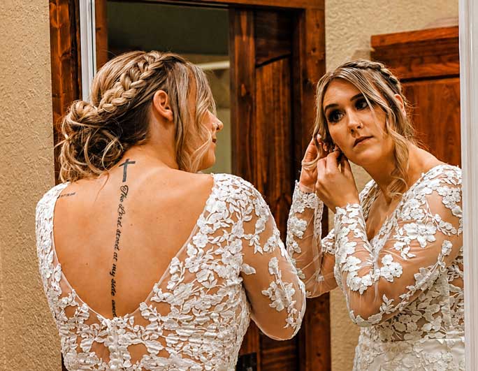 Bride adjusting her earrings in the Willowood Ranch bridal suite mirror before her wedding ceremony