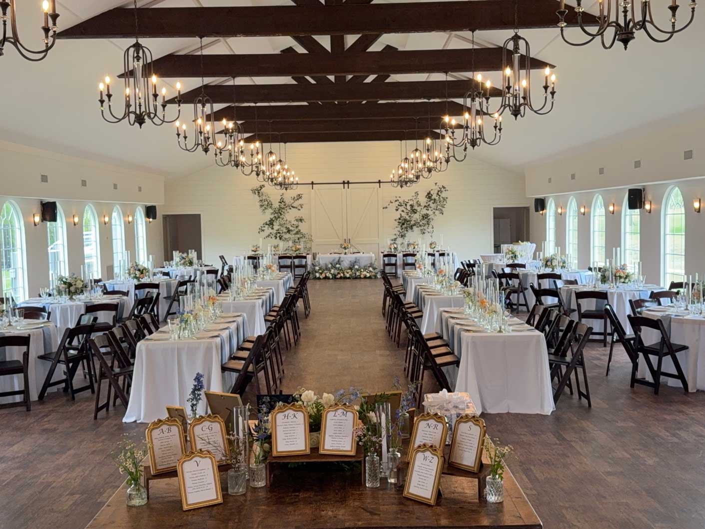 Wedding reception layout inside Willowood Ranch event center with long tables, chandeliers, and vaulted ceilings in North Texas