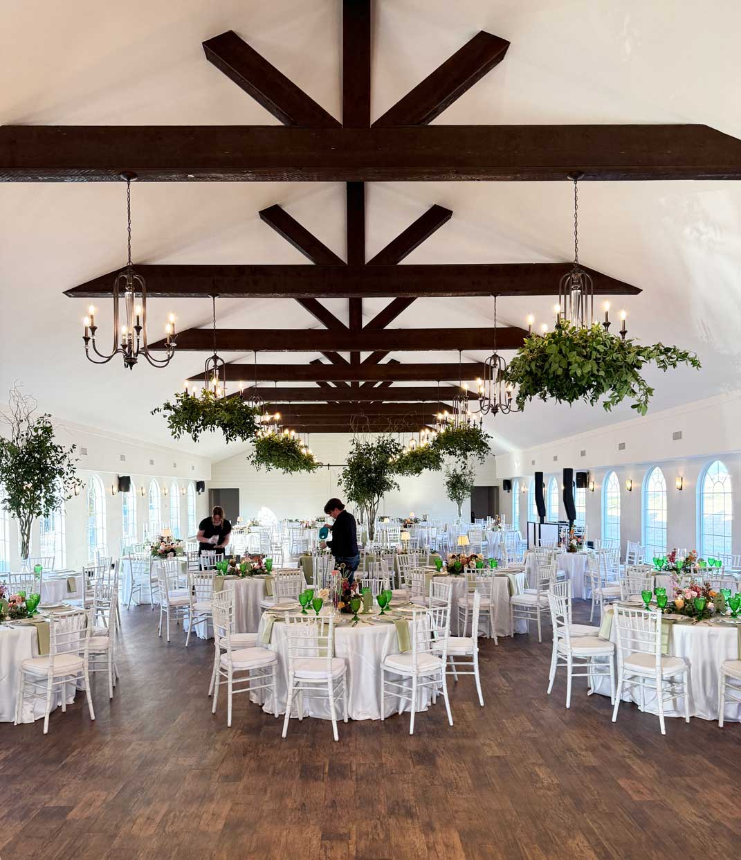 Wedding reception setup inside Willowood Ranch event center with round tables, chandeliers, and wood beam ceiling in North Texas