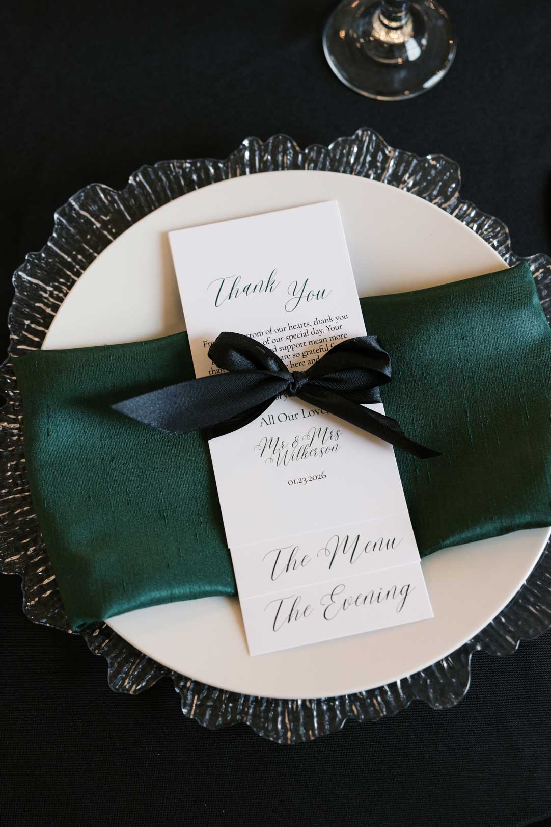 Modern wedding place setting with green napkin, black ribbon, and printed menu at Willowood Ranch Event Center