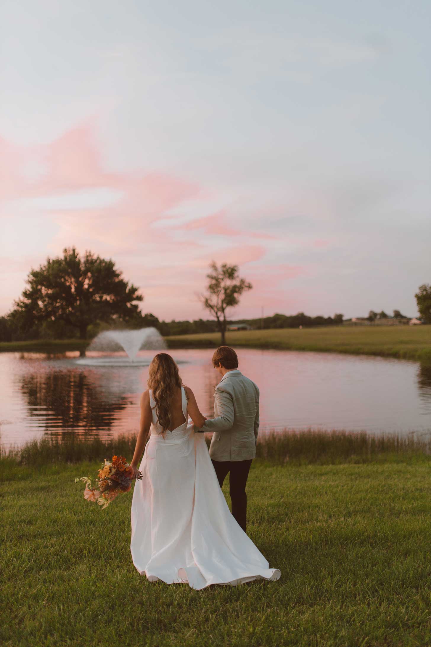 Bride and groom walking by pond at sunset on Willowood Ranch grounds after wedding ceremony in Bells Texas