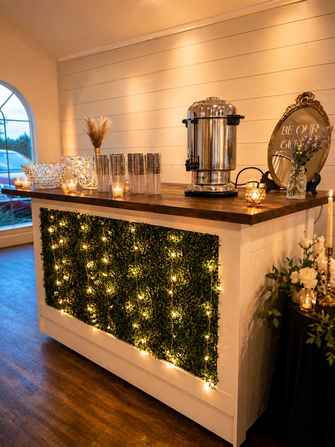 Warmly lit wedding reception beverage station with coffee service, glassware, and decorative greenery at Willowood Ranch event center in North Texas