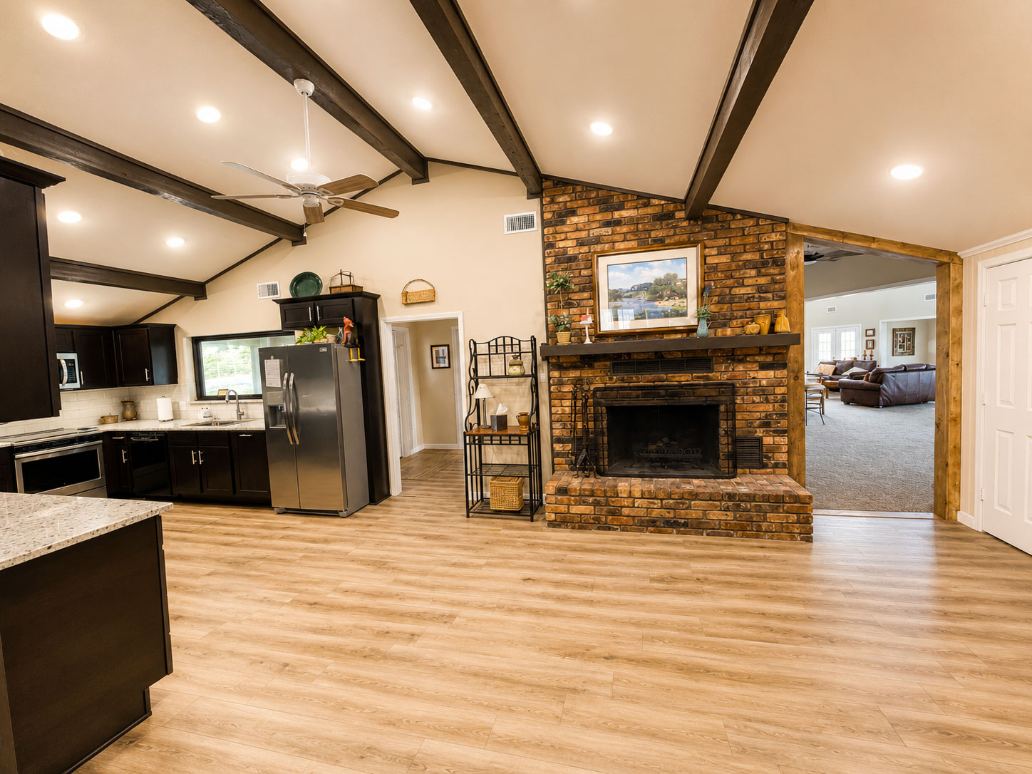 Open-concept Ranch House kitchen and great room with vaulted ceilings, brick fireplace, and rustic wood beams at Willowood Ranch in Bells, Texas.