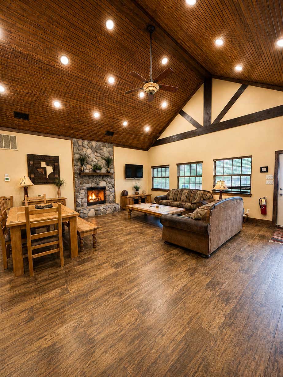 Lone Star Great Room with Stone Fireplace | Willowood Ranc Great room inside the Lone Star cabin at Willowood Ranch featuring vaulted wood ceilings, a stone fireplace, comfortable seating, dining area, and rustic lodge-style design.